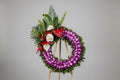 A large floral wreath made of purple orchids and green foliage, decorated with red and white flowers, displayed on a stand in a florist shop.