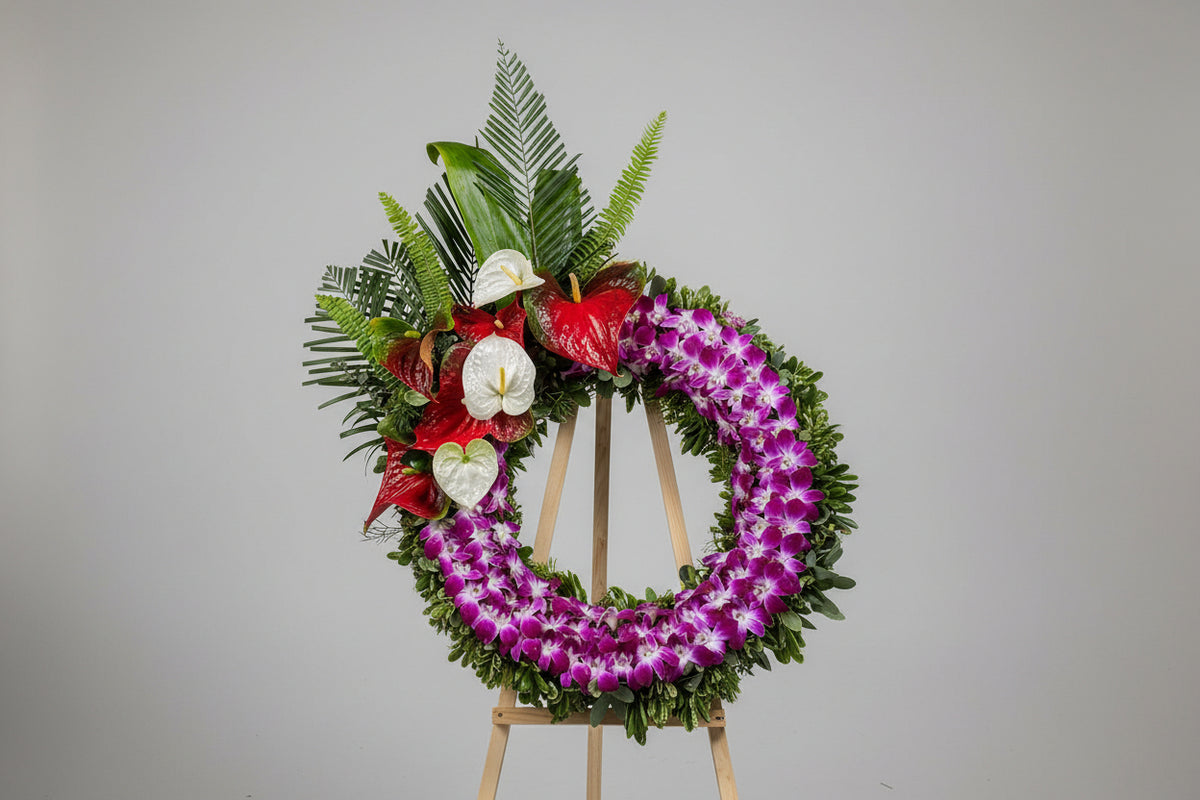 A large floral wreath made of purple orchids and green foliage, decorated with red and white flowers, displayed on a stand in a florist shop.